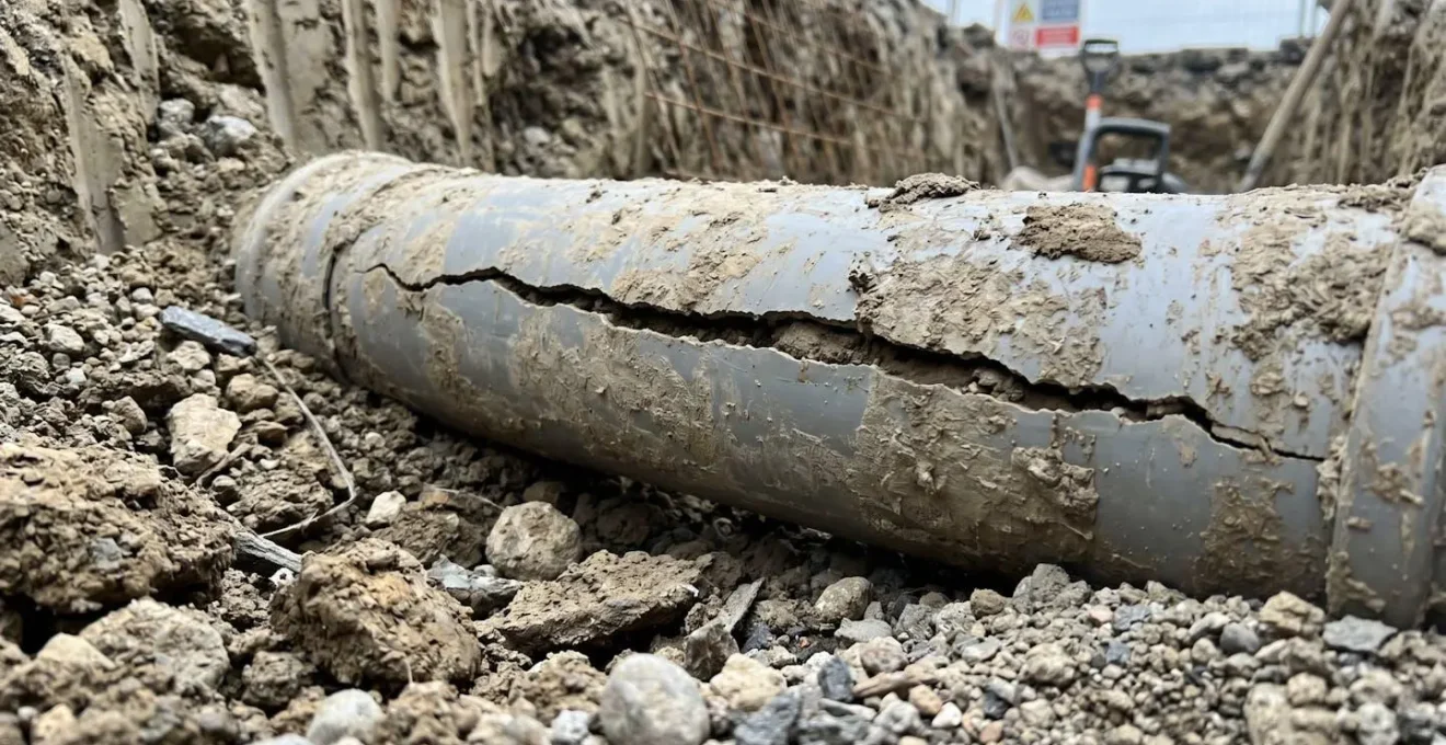 Section de canalisation PVC ancienne partiellement visible dans le sol montrant une fissure longitudinale